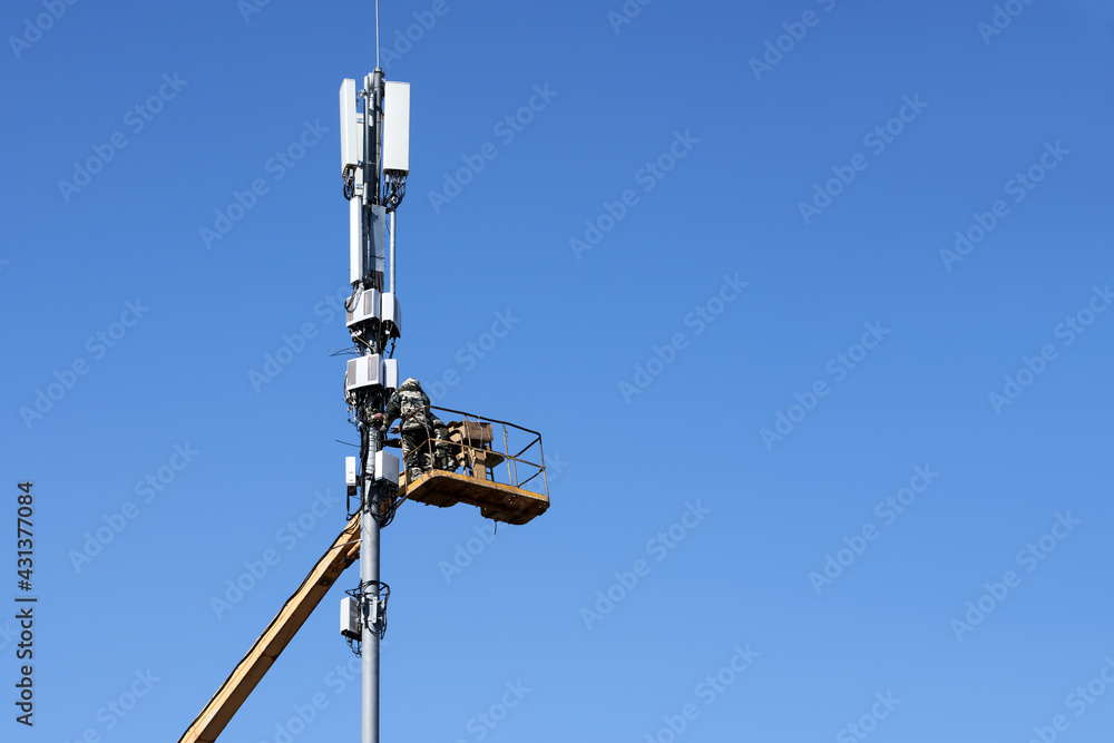 Communication engineers from the lifting cradle install the honeycombs on the cellular communication mast. Copy space.