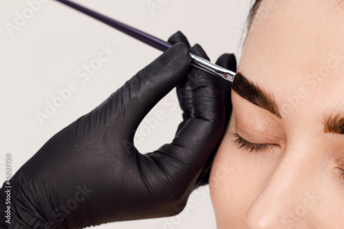 Master applies brow paste with a brush to eyebrows. Styling and lamination of eyebrows. Woman doing eyebrow permanent makeup correction. Eyebrow shaping with a cosmetic brush close-up.