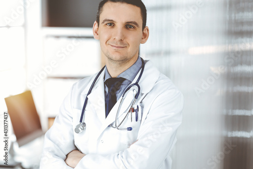 Male doctor standing straight with arms crossed in clinic near his working place. Perfect medical service in hospital. Medicine and healthcare concept
