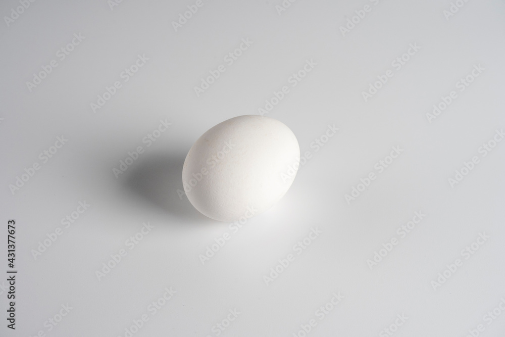 a white chicken egg lies on a white background. Minimalistic still life a white chicken egg lies on a white background. Minimalistic still life