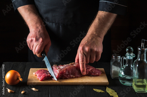 Chef or cook cutting beef meat with knife on kitchen, cooking food. Vegetables and spices on kitchen table to prepare delicious lunch