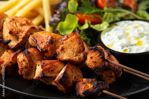 Chicken fillet souvlaki, kebabs on skewers with potato chips, salad and fresh home made tzatziki
