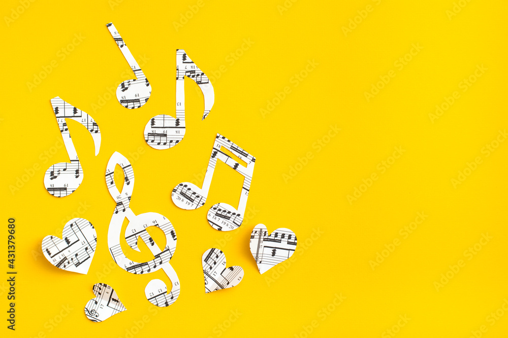 Musical notes, clef and hearts cut from paper with musical text on yellow background. Copy space Musical notes, clef and hearts cut from paper with musical text on yellow background. Copy space