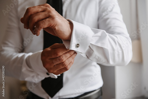 the groom fastens a button on the sleeve of his shirt