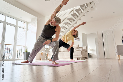 Fit middle aged 50s family couple doing fitness yoga morning exercise at home. Sporty healthy old mature man and woman training together standing in living room. Active seniors sport stretching. photo