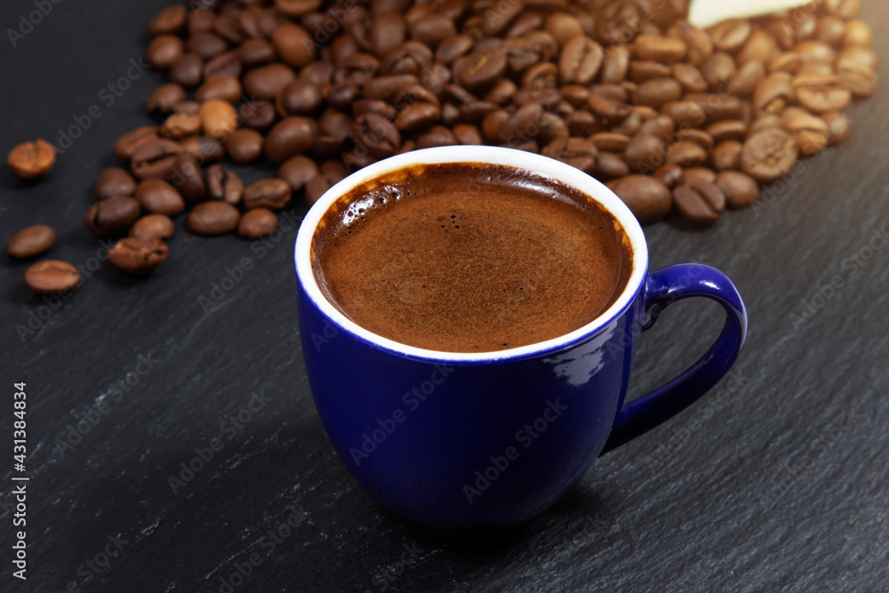 Fototapeta premium Dark coffee in a blue cup on a background of coffee beans