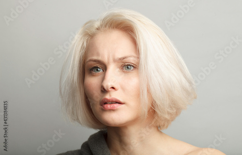 Foto skeptic young beautiful blonde female model on gray background