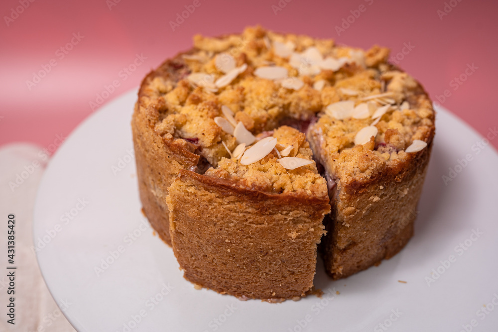 A round cake with almonds on a white plate on a pink surface