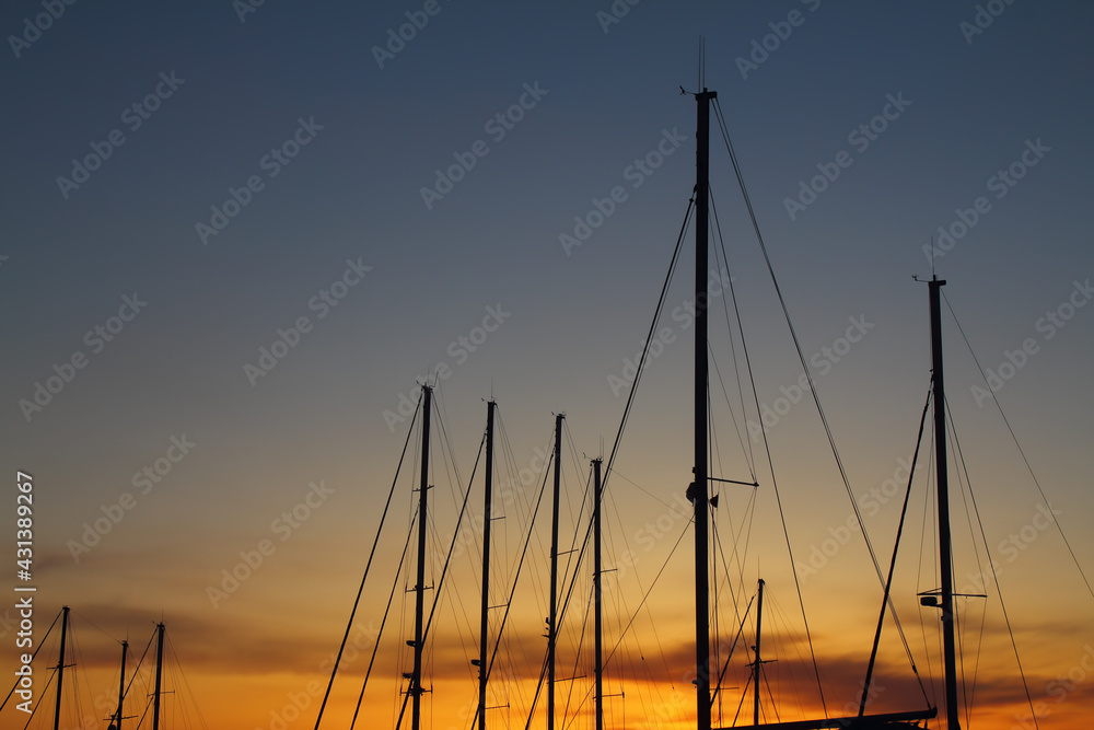 Fiery contrasting clouds in the blue sky, at sunset, through the masts of sailing yachts.