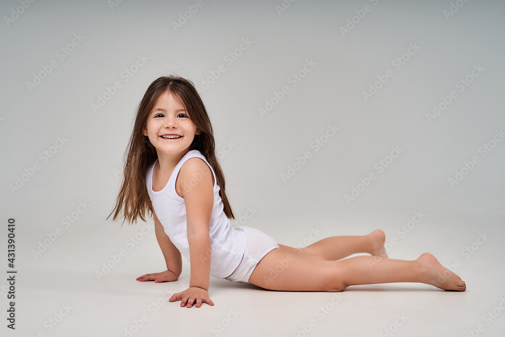 Foto de A little girl on a white background in a white T-shirt and white  panties smiles do Stock