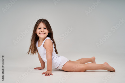 A little girl on a white background in a white T-shirt and white panties smiles