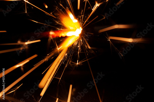 horizontal close-up conceptual photography of a bright burning sparkler fire with bright hot orange and yellow sparks trails in the darkness