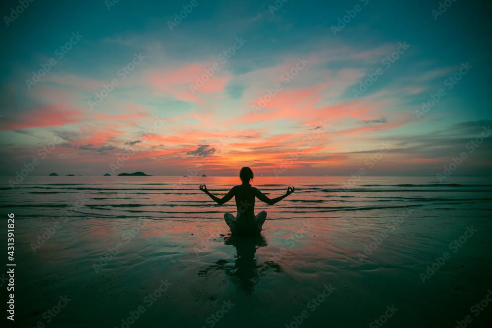 Silhouette of fitnes woman practicing yoga on the sea beach at amazing sunset.