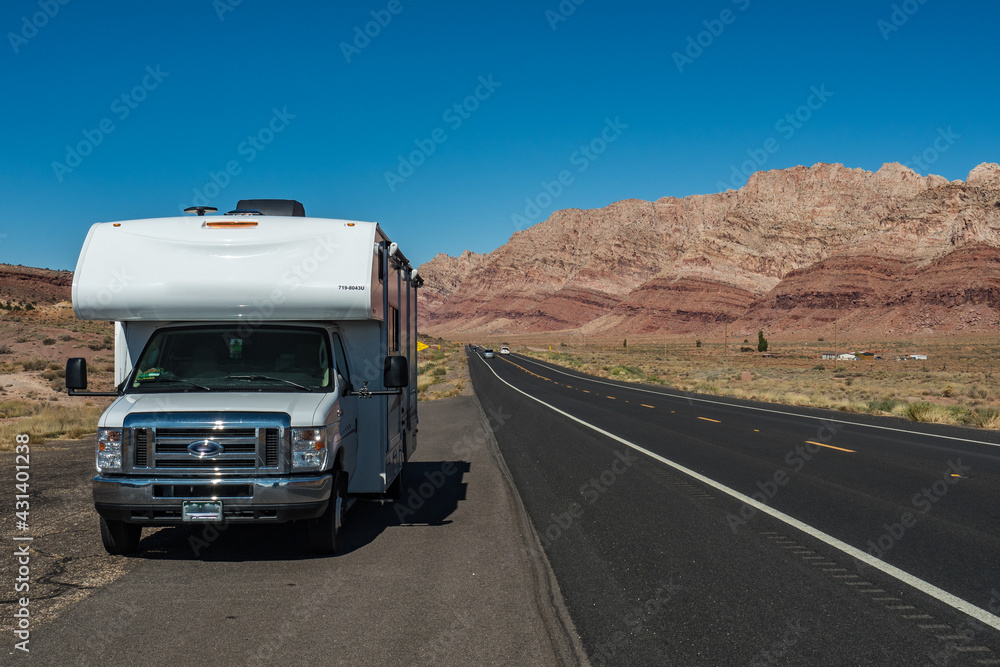 C-type camper with slideouts standing in the desert on the side of the road with mountains in the background and a highway passing