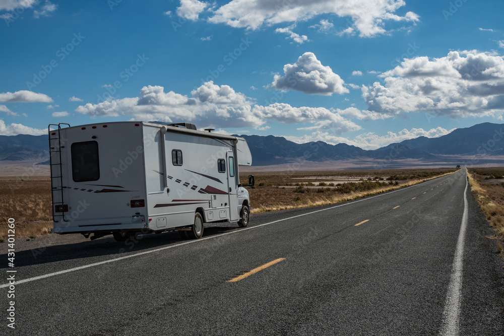 C-type camper with slideouts standing in the desert on the side of the road with mountains in the background and a highway passing