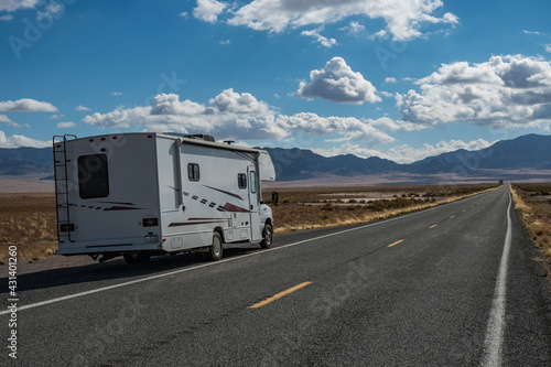 C-type camper with slideouts standing in the desert on the side of the road with mountains in the background and a highway passing © Markus