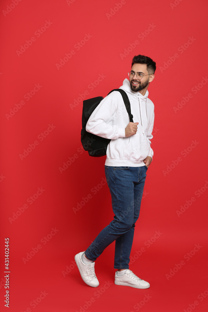 Young man with stylish backpack walking on red background Young man with stylish backpack walking on red background