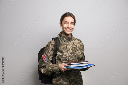 Fotografija Female cadet with backpack and books on light grey background
