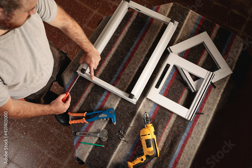 Top view of man working in a carpentry shop. Assembling a white aluminum window. Horizontal image.
