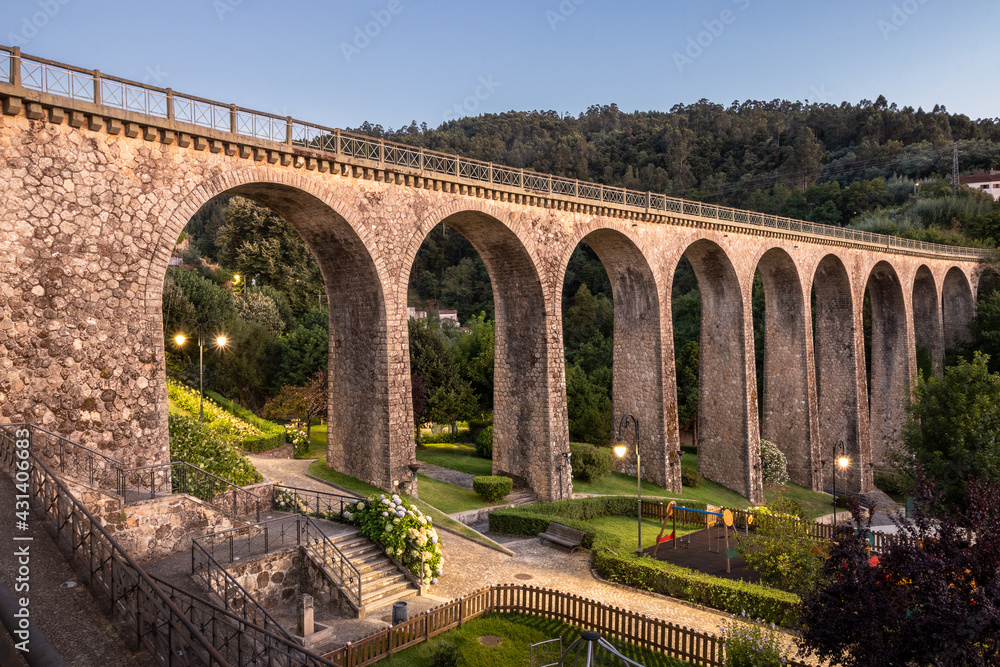 Old railway bridge and garden in Vouzela, Portugal, after sunset on a summer day.