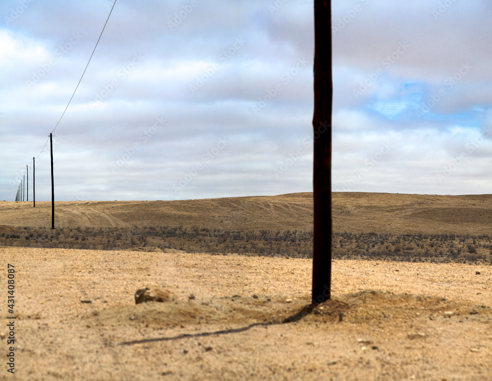 Arid flat and desolate scenic landscape in Namibia on the way to Swakopmund with electric pylons and cloudy sky. (Selective focus)