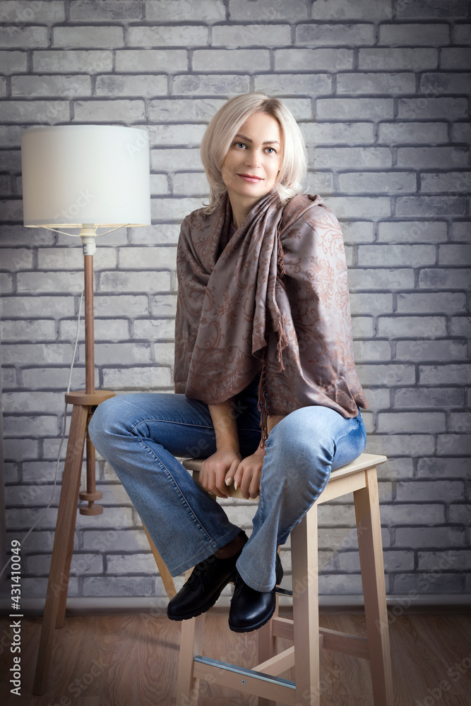 Beautiful blond mature woman posing sitting on bar stool at home or bar.