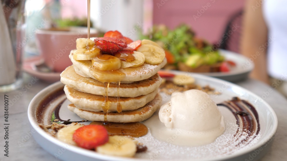 Sweet american breakfast. Pouring syrup over stack of fluffy pancakes served with scoop of ice cream and berries Sweet american breakfast. Pouring syrup over stack of fluffy pancakes served with scoop of ice cream and berries