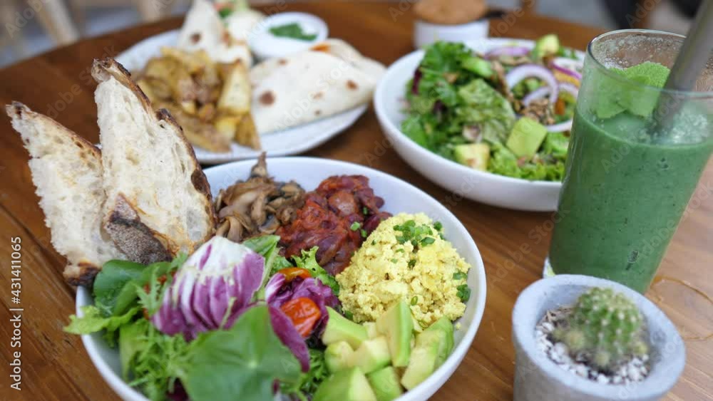 Vegan lunch for friends of buddha bowls, greens, tofu omelette and potato wings served on a wooden table Vegan lunch for friends of buddha bowls, greens, tofu omelette and potato wings served on a wooden table