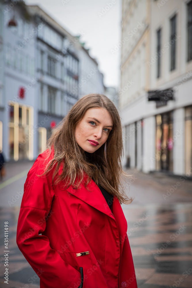 Fototapeta premium Beautiful girl posing in the city center dressed in a red coat.Beautiful girl posing in the city center dressed in a red coat. Model walks through the streets of the city.