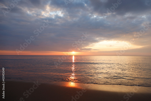 Beautiful sunset over the clam sea with cloud sky background. Sunset over tropical beach. Nature summer concept. Peak sunset over sea with yellow light reflect on sea water. Tranquil seascape. 