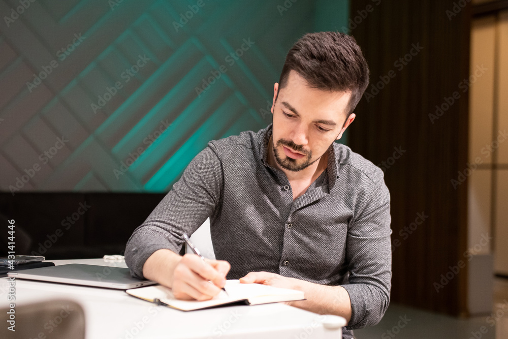 Young bearded man writes in a diary while working from home. Remote job. Young bearded man writes in a diary while working from home. Remote job.