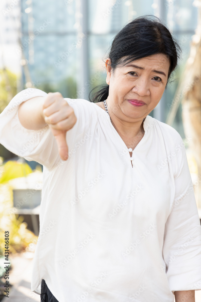 Unhappy old asian senior woman giving negative, no, bad, rejecting thumb down gesture Unhappy old asian senior woman giving negative, no, bad, rejecting thumb down gesture