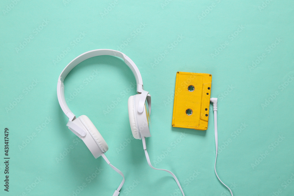 Stereo headphones with audio cassette on mint green background. Retro 80s still life. Top view Stereo headphones with audio cassette on mint green background. Retro 80s still life. Top view