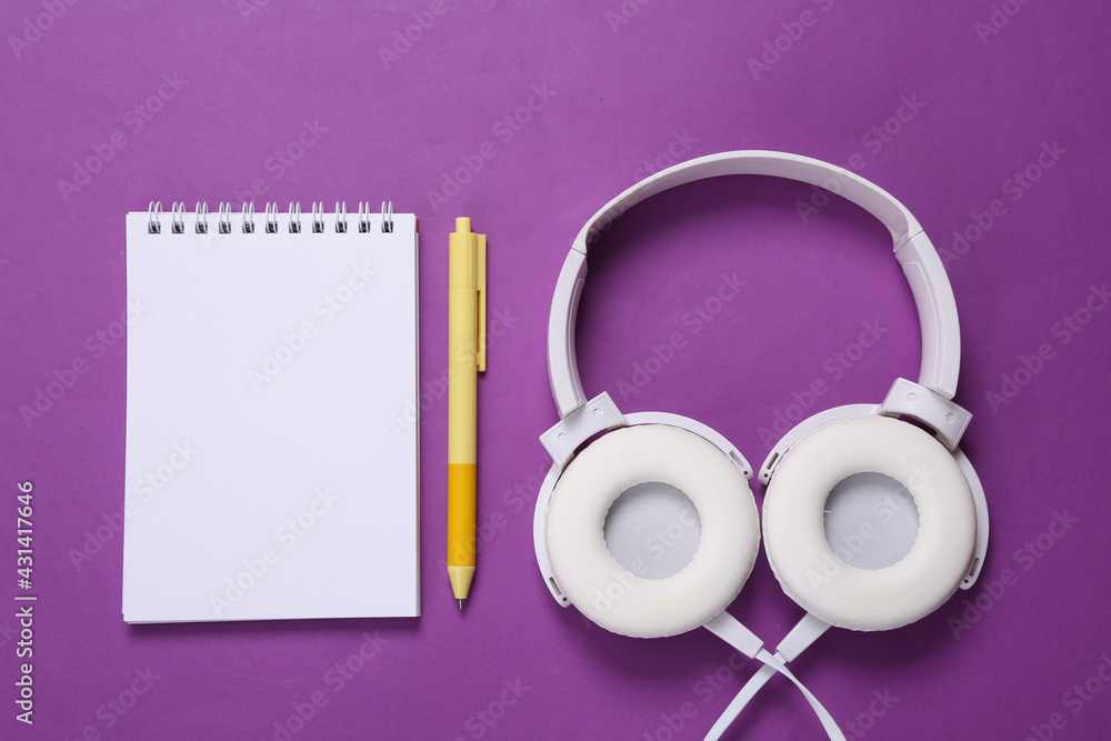 Stereo headphones and blank notebook for copy space on purple background. Fitness concept. Training plan Stereo headphones and blank notebook for copy space on purple background. Fitness concept. Training plan