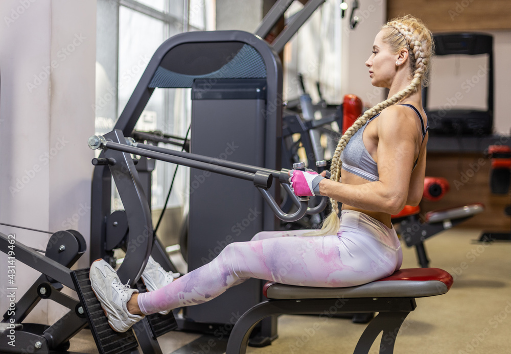 Obraz premium Young attractive woman in sportswear trains back muscles in exercise machine at gym