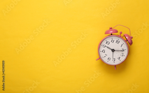 Pink alarm clock on yellow background. Copy space. Top view. Flat lay