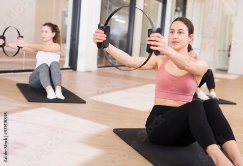 Young sporty woman doing exercises with pilates circle during group training at fitness center