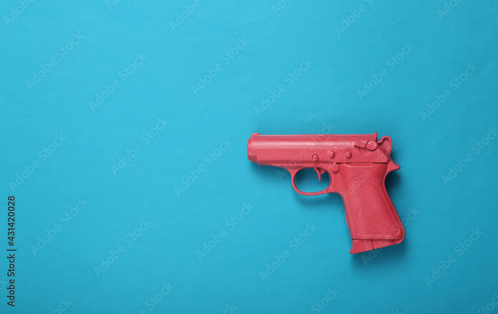 Pink pistol gun on blue background. Creative concept. Minimalism Flat lay. Minimal layout.Top view Pink pistol gun on blue background. Creative concept. Minimalism Flat lay. Minimal layout.Top view