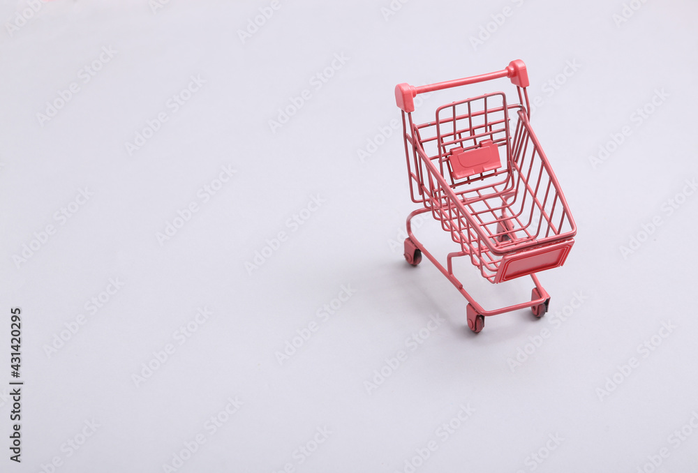 Mini pink supermarket trolley on gray background. Shopping concept