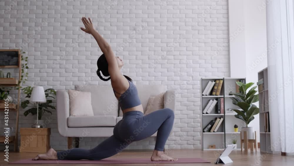 Asian woman look laptop practice yoga warrior pose online course at home