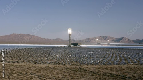 Aerial Moving Forward Across The Desert To A Solar Field, With Dirt, Dry Brush, Clear Blue Sky, Bright Sunlight, And Steep Mountains In The Background - Ivanpah, California photo