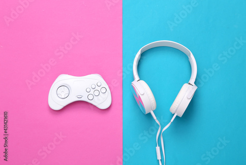 Creative gaming layout. White Retro gamepad and headphones on a blue-pink background. Top view, Flat lay. Concept art