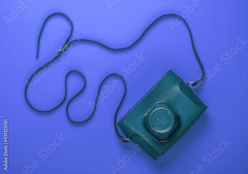 Retro camera in a leather case with strap on blue background. Top view