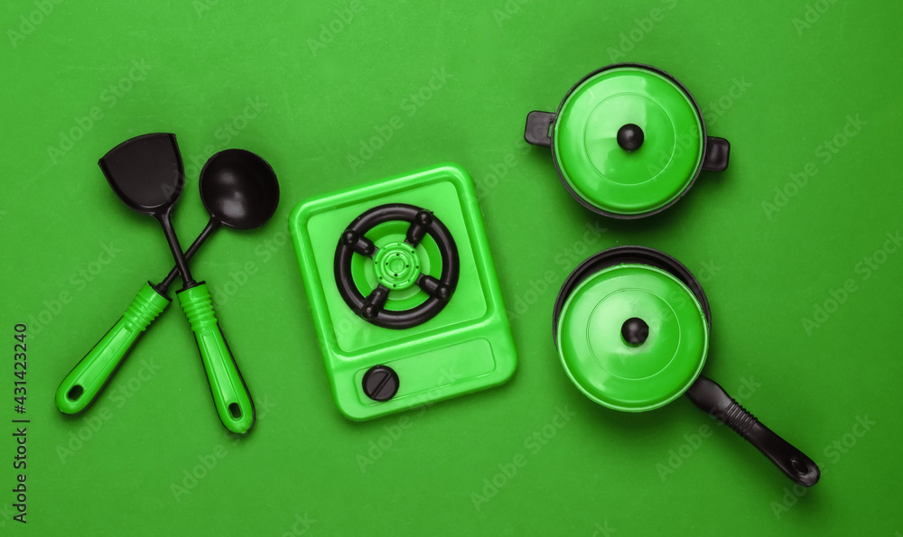 Toy set of children's kitchen on green background. Pots, kitchen tools, stove. Top view Toy set of children's kitchen on green background. Pots, kitchen tools, stove. Top view