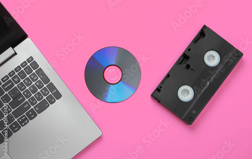 Flat lay composition of laptop, cd disc, audio cassette on pink background. Retro storage media. Top view