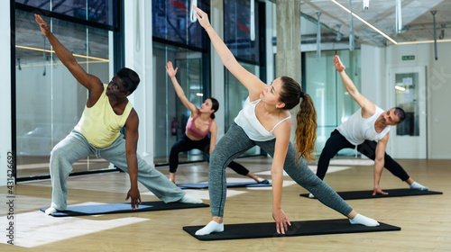 Group of young adults maintaining active lifestyle exercising during pilates class in modern fitness center