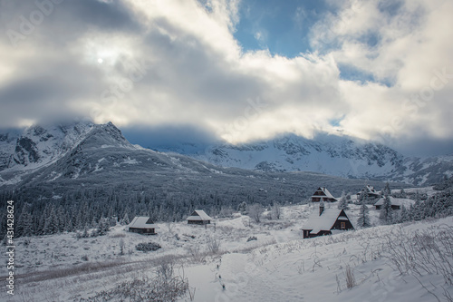 Hala Gąsienicowa Valley in winter, Tatra Mountains, Poland. Small wooden chalets, white snow and dramatic clouds over the area. Selective focus on the details, blurred background.
