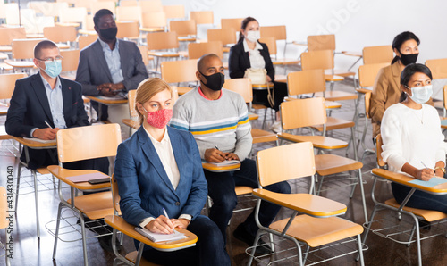 Multiethnic group of people wearing protective masks sitting in conference room keeping distance during business training. Precautions during mass events in coronavirus pandemic