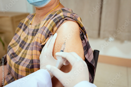 Close up on doctor is injecting vaccination on senior woman arm. Adult patient wearing protective face mask for protect Coronavirus Covid-19 pandemic. Health care and medical concept.