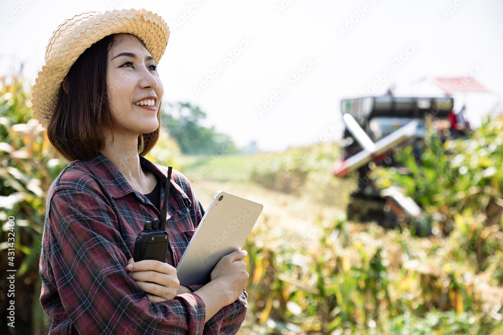 Asian beautiful farmer using walkie talkie and tablet to control harvesting corn with tractor in corn fields. Concepts and perspectives on agricultural success
